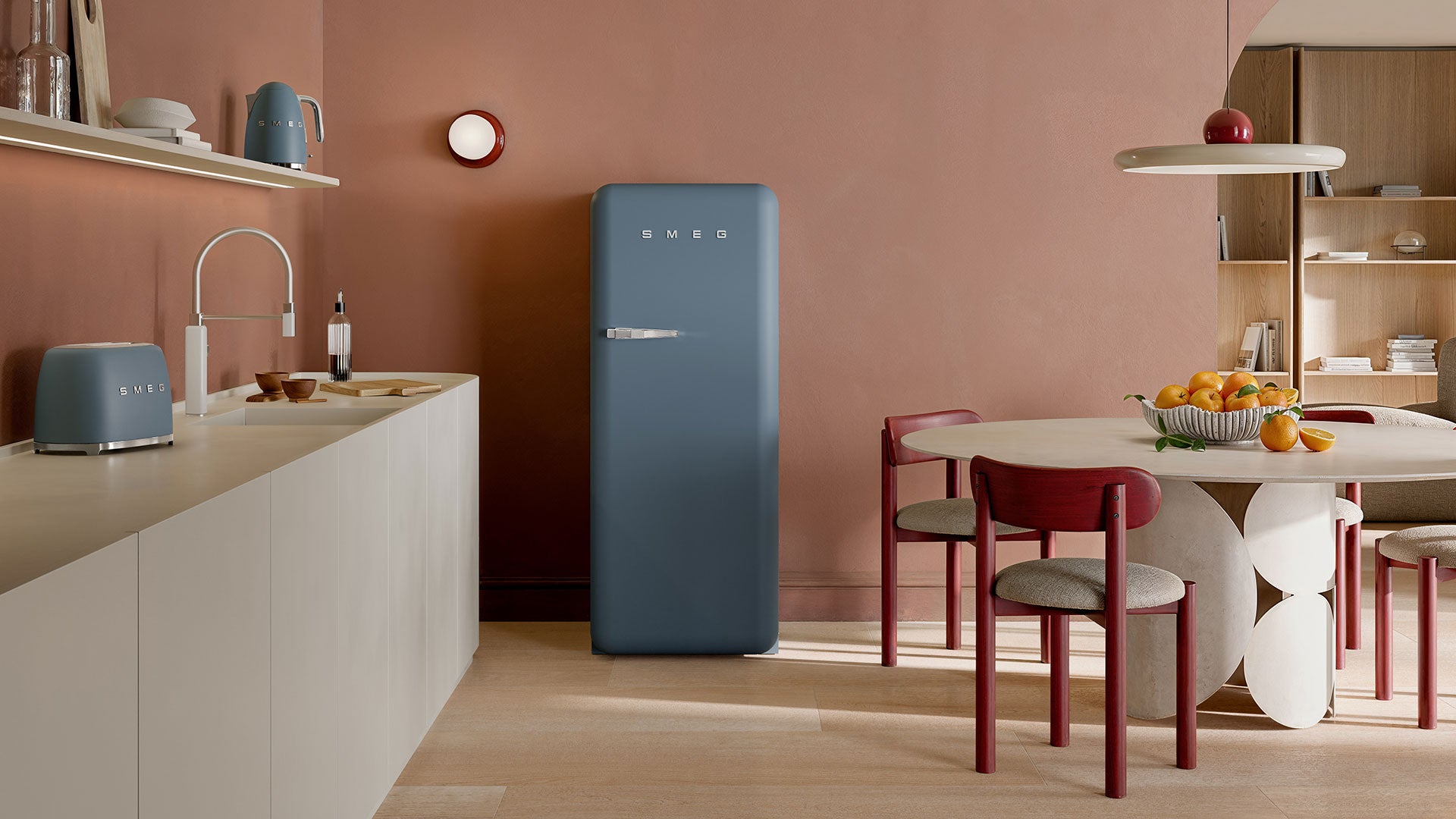 Modern kitchen with a storm blue Smeg refrigerator, kettle, toaster, and dining area.