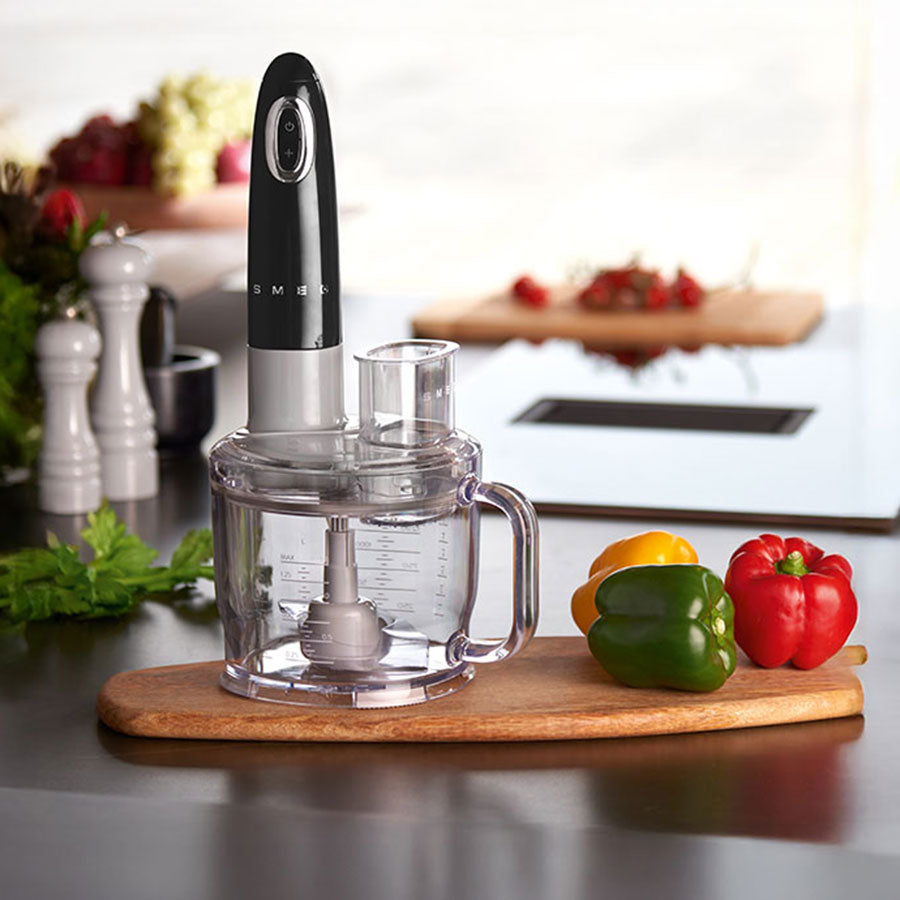 Smeg food processor on a kitchen counter with peppers and a cutting board.