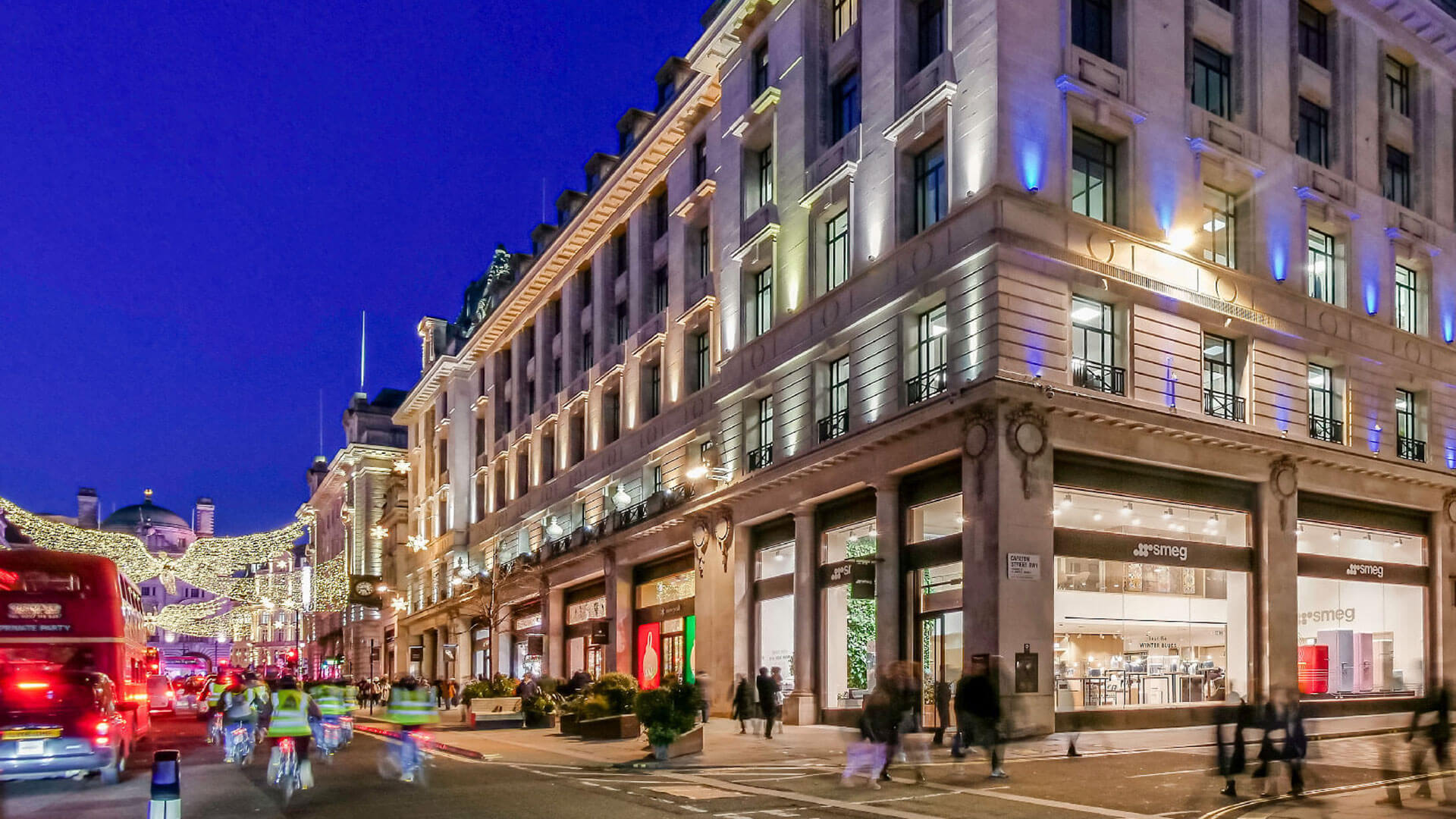 City street scene with illuminated buildings and people walking at night.